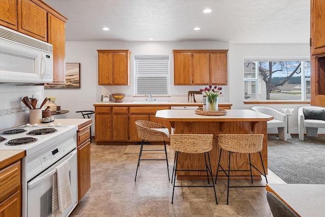 2603 S Sunnybrook Ln, Spokane, WA 99037 - kitchen with white appliances, light countertops, a breakfast bar area, brown cabinets, and recessed lighting