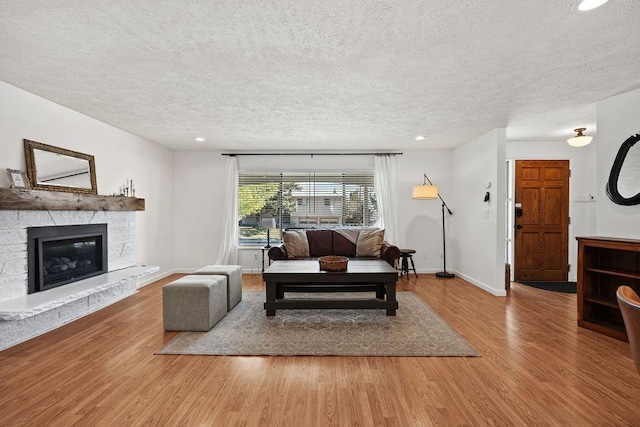 living room featuring a textured ceiling, a stone fireplace, recessed lighting, wood finished floors, and baseboards