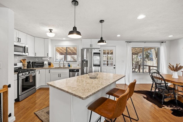 kitchen with a sink, light wood-style flooring, decorative backsplash, and stainless steel appliances