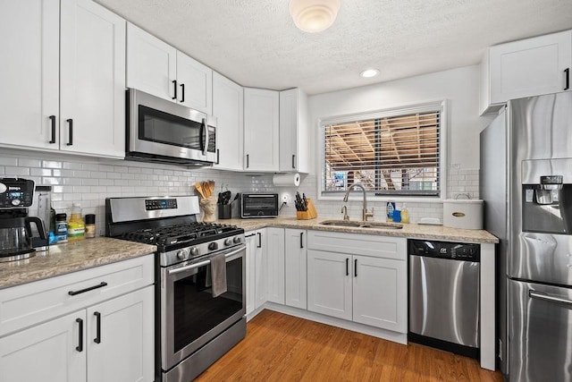 kitchen with light wood-type flooring, white cabinets, appliances with stainless steel finishes, a sink, and backsplash