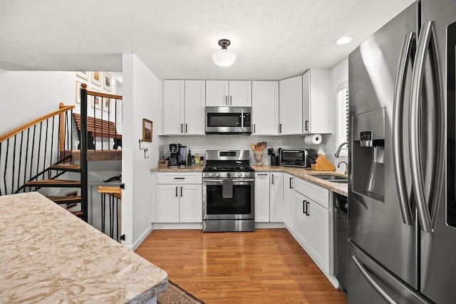 kitchen featuring white cabinets, a sink, appliances with stainless steel finishes, light wood finished floors, and decorative backsplash