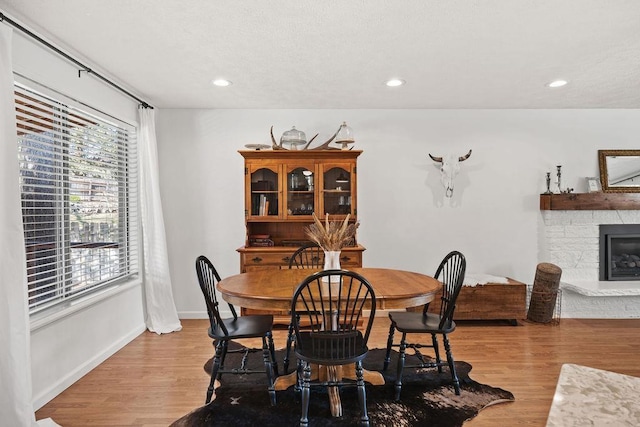 dining area featuring light wood finished floors, a stone fireplace, and recessed lighting