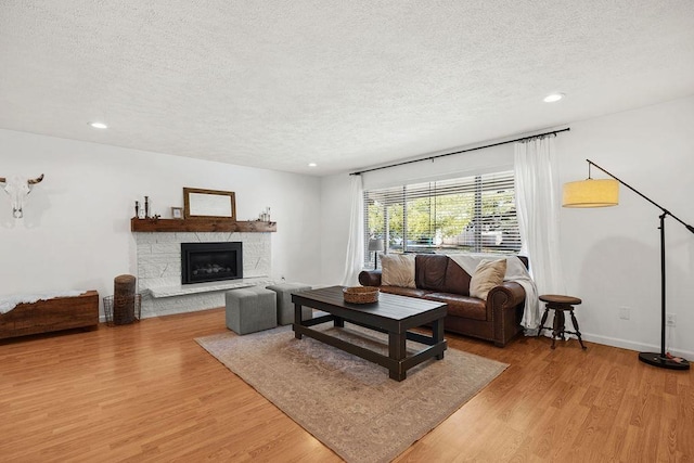 living room with baseboards, a fireplace, a textured ceiling, recessed lighting, and light wood finished floors