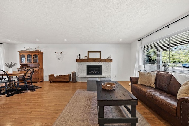 living area with a stone fireplace, baseboards, recessed lighting, a textured ceiling, and wood finished floors