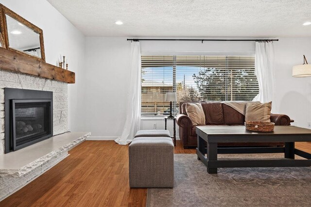 living area featuring baseboards, a stone fireplace, a textured ceiling, recessed lighting, and wood finished floors