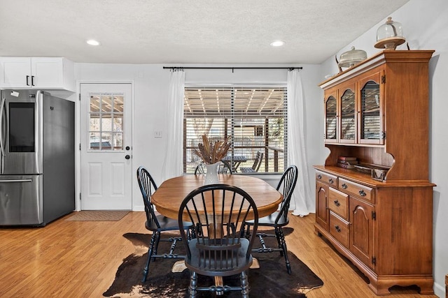 dining space featuring light wood-style flooring, a textured ceiling, and a healthy amount of sunlight