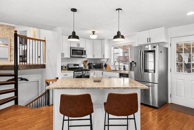 kitchen featuring white cabinets, a sink, light wood finished floors, stainless steel appliances, and a breakfast bar area