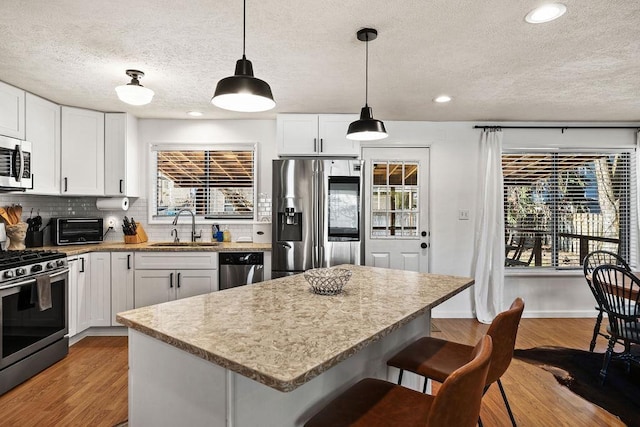 kitchen with a sink, a breakfast bar, wood finished floors, stainless steel appliances, and decorative backsplash