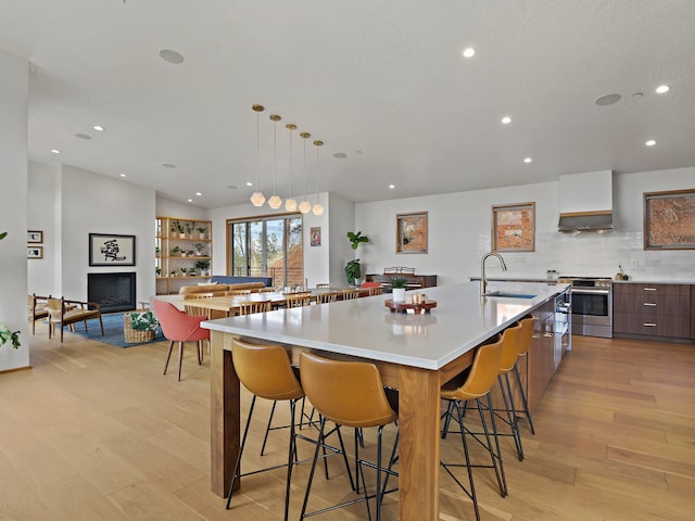 kitchen with modern cabinets, wall chimney range hood, a large island, a sink, and stainless steel range