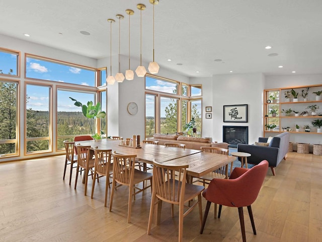 dining room featuring light wood-style flooring, a glass covered fireplace, and recessed lighting