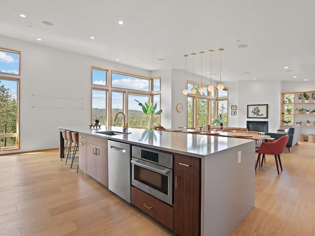 kitchen with modern cabinets, a large island with sink, a sink, stainless steel appliances, and light wood finished floors