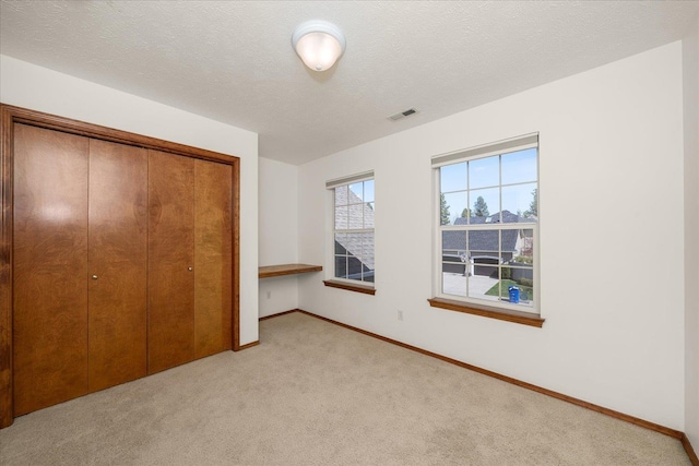 unfurnished bedroom featuring a closet, visible vents, light carpet, baseboards, and a textured ceiling