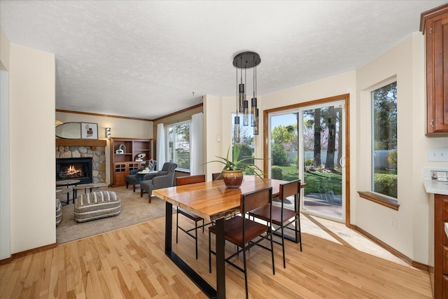 dining room with light wood finished floors, a textured ceiling, baseboards, and a fireplace