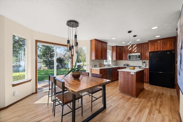 kitchen with stainless steel appliances, a kitchen island, light countertops, light wood finished floors, and a sink