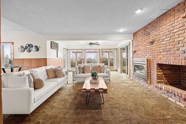 living room with carpet flooring, a brick fireplace, a textured ceiling, and a wainscoted wall