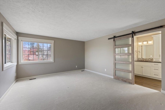 unfurnished bedroom featuring carpet floors, baseboards, a barn door, and visible vents