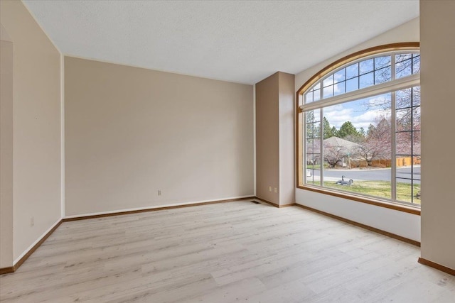 spare room with baseboards, light wood-style floors, and a textured ceiling