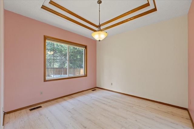 spare room featuring light wood finished floors, visible vents, baseboards, and a raised ceiling