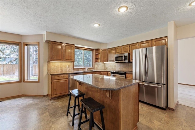 kitchen featuring a kitchen bar, tasteful backsplash, appliances with stainless steel finishes, a sink, and brown cabinets