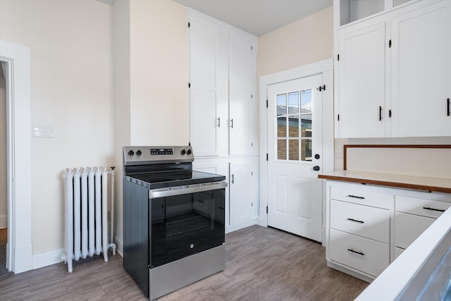 kitchen with radiator, baseboards, stainless steel range with electric stovetop, and white cabinets