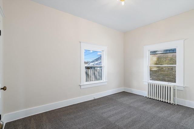 spare room featuring radiator heating unit, dark colored carpet, and baseboards