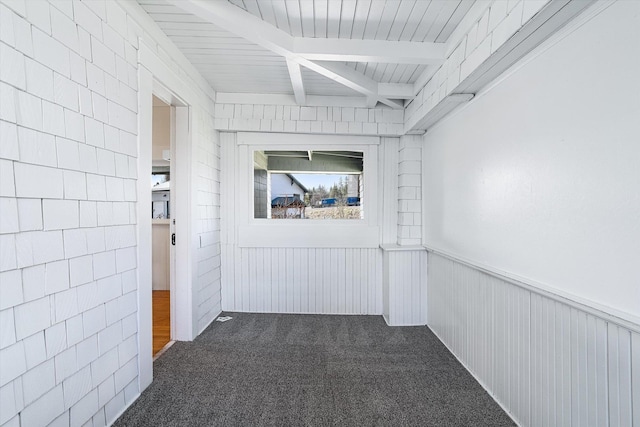 empty room with carpet flooring, wainscoting, and beam ceiling