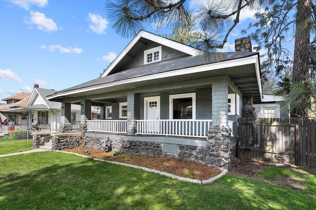 view of front facade featuring a porch, a front lawn, fence, and a chimney