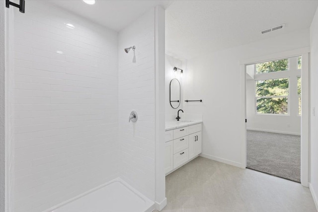 bathroom with a tile shower, baseboards, vanity, and visible vents