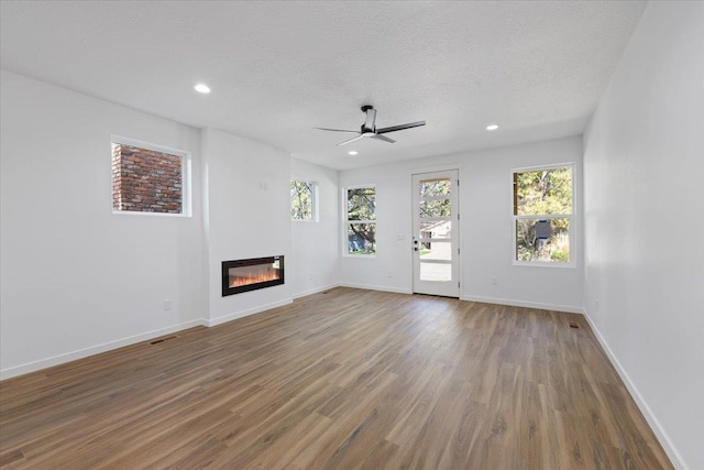 unfurnished living room featuring a glass covered fireplace, wood finished floors, ceiling fan, baseboards, and recessed lighting