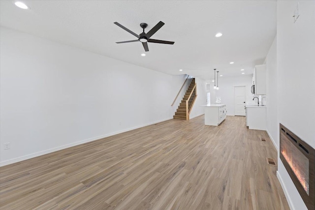 unfurnished living room featuring stairs, light wood-style flooring, recessed lighting, a ceiling fan, and a sink