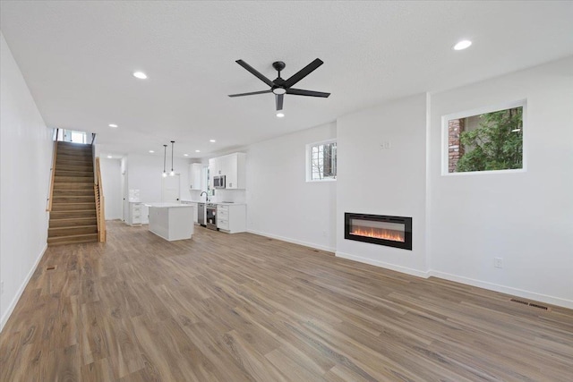 unfurnished living room featuring baseboards, light wood-style floors, a glass covered fireplace, and ceiling fan