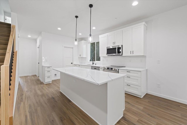 kitchen with appliances with stainless steel finishes, a sink, wood finished floors, white cabinetry, and a center island