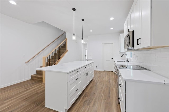 kitchen featuring stainless steel microwave, light wood-style flooring, a sink, and range with electric stovetop