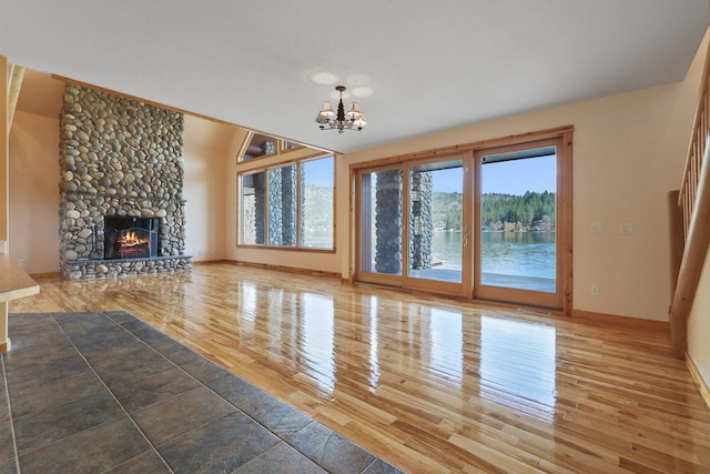 unfurnished living room with a stone fireplace, an inviting chandelier, and wood finished floors