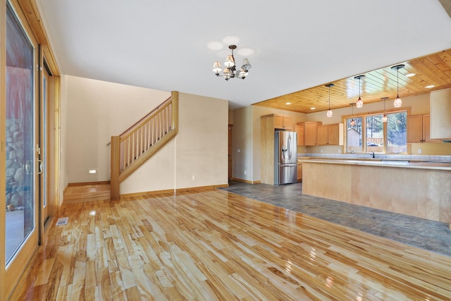 kitchen with an inviting chandelier, light brown cabinetry, stainless steel refrigerator with ice dispenser, light countertops, and light wood finished floors