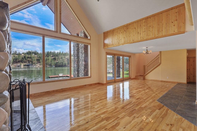 unfurnished living room featuring high vaulted ceiling, baseboards, a chandelier, and wood finished floors