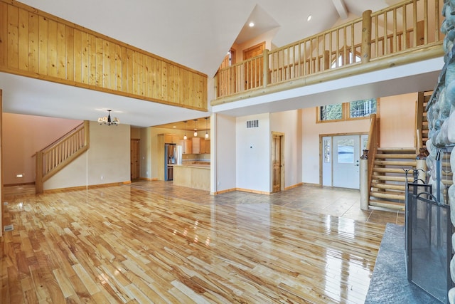 unfurnished living room with stairs, a notable chandelier, visible vents, and light wood-type flooring