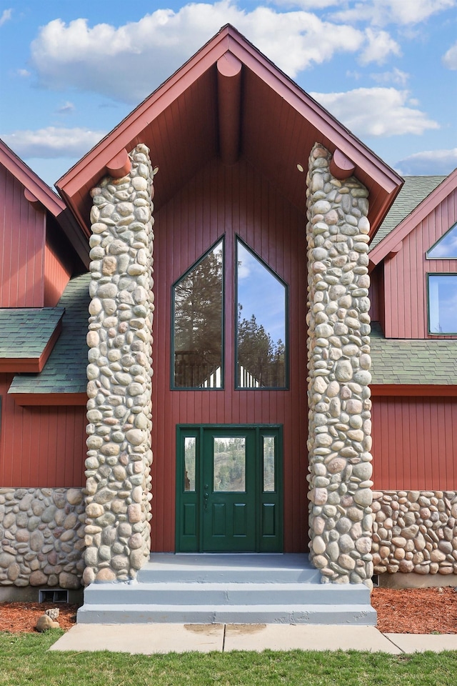 entrance to property featuring a shingled roof and stone siding