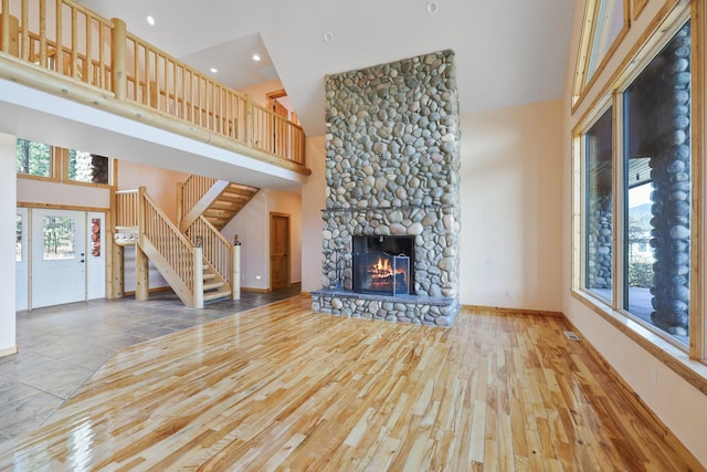 unfurnished living room featuring a towering ceiling, a stone fireplace, wood finished floors, stairs, and baseboards