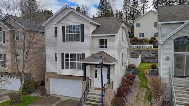 traditional home featuring central AC, driveway, a garage, and roof with shingles