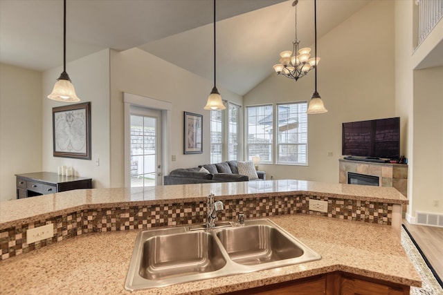 kitchen with visible vents, light stone counters, a sink, open floor plan, and decorative light fixtures