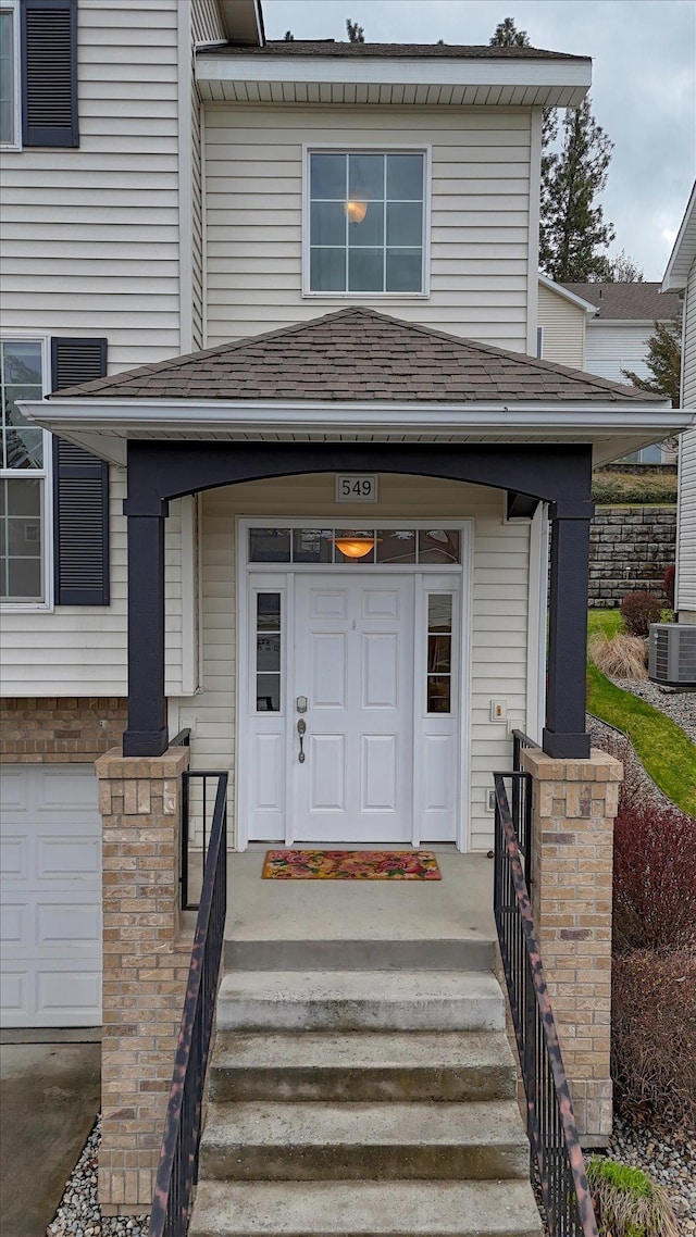 property entrance featuring a shingled roof, covered porch, and a garage