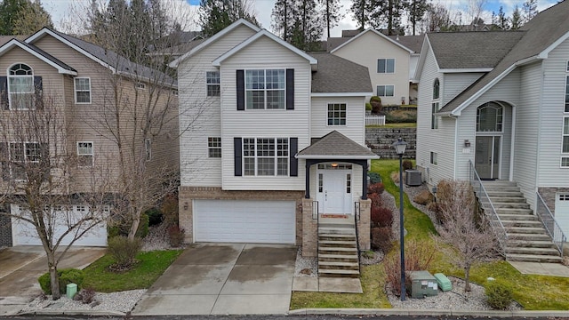 view of front of home featuring cooling unit, roof with shingles, brick siding, an attached garage, and driveway