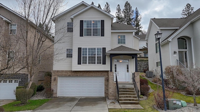 traditional-style house with central AC unit, a shingled roof, an attached garage, concrete driveway, and brick siding