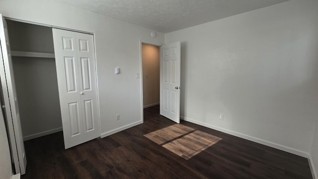 unfurnished bedroom featuring a closet, dark wood-style floors, a textured ceiling, and baseboards
