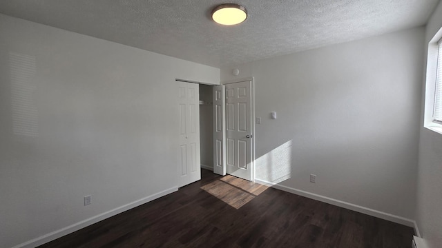 unfurnished bedroom with a textured ceiling, a closet, a baseboard heating unit, baseboards, and dark wood-style floors