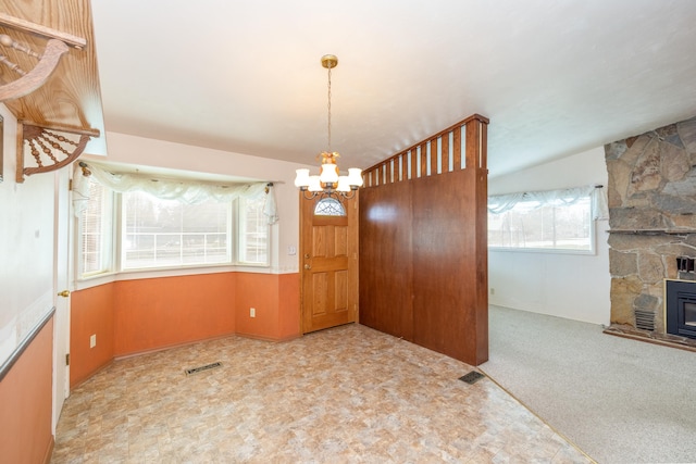 unfurnished dining area with carpet, an inviting chandelier, a stone fireplace, and visible vents