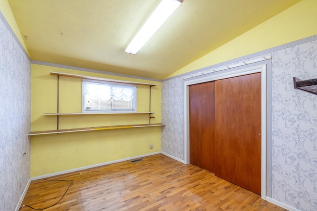 unfurnished bedroom with a closet, wallpapered walls, visible vents, lofted ceiling, and wood finished floors
