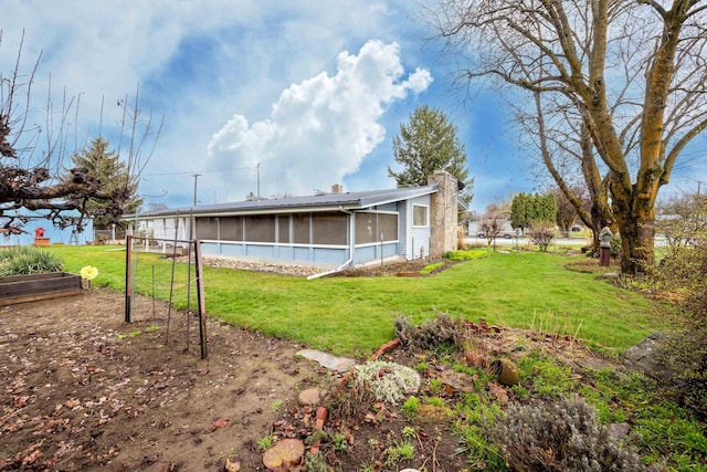 rear view of property with a garden, a chimney, a sunroom, and a lawn