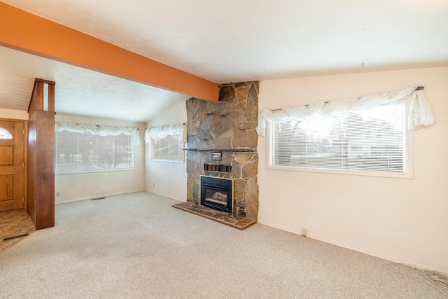 unfurnished living room with visible vents, a stone fireplace, vaulted ceiling with beams, and carpet flooring